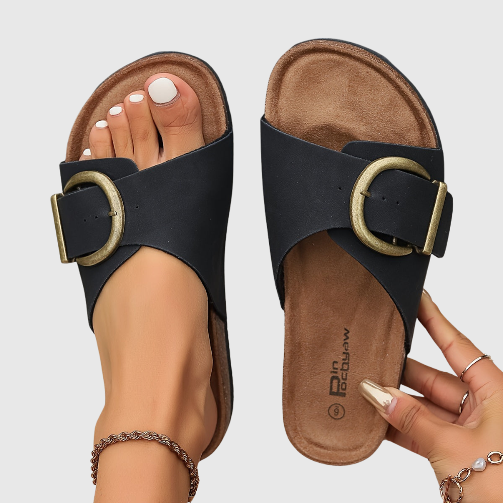 Black sandals with gold buckles on a neutral background