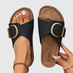 Black sandals with gold buckles on a neutral background