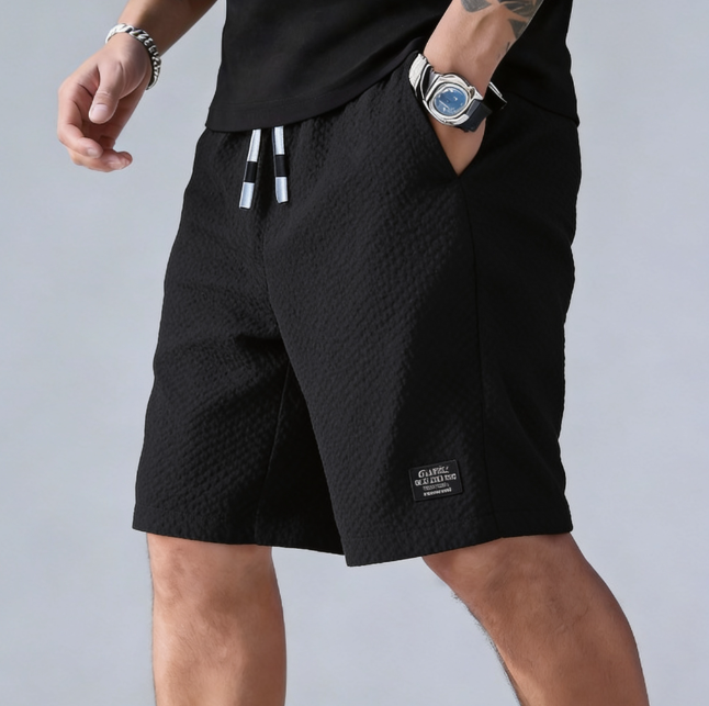 Person wearing black shorts with a brand logo on a gray background