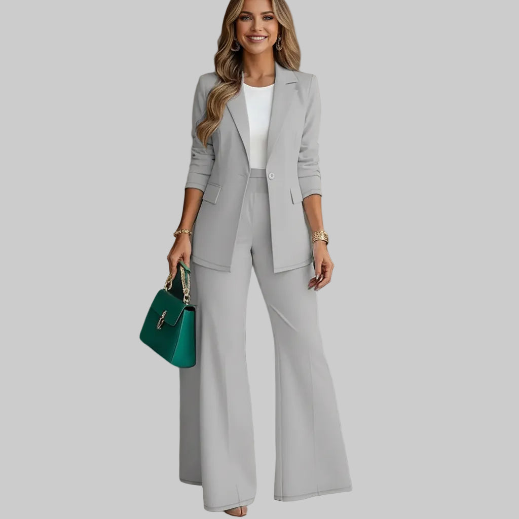 Woman in a gray suit with a teal handbag standing against a neutral background