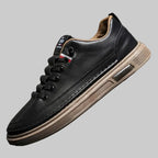 Black leather sneaker with brown accents on a gray background