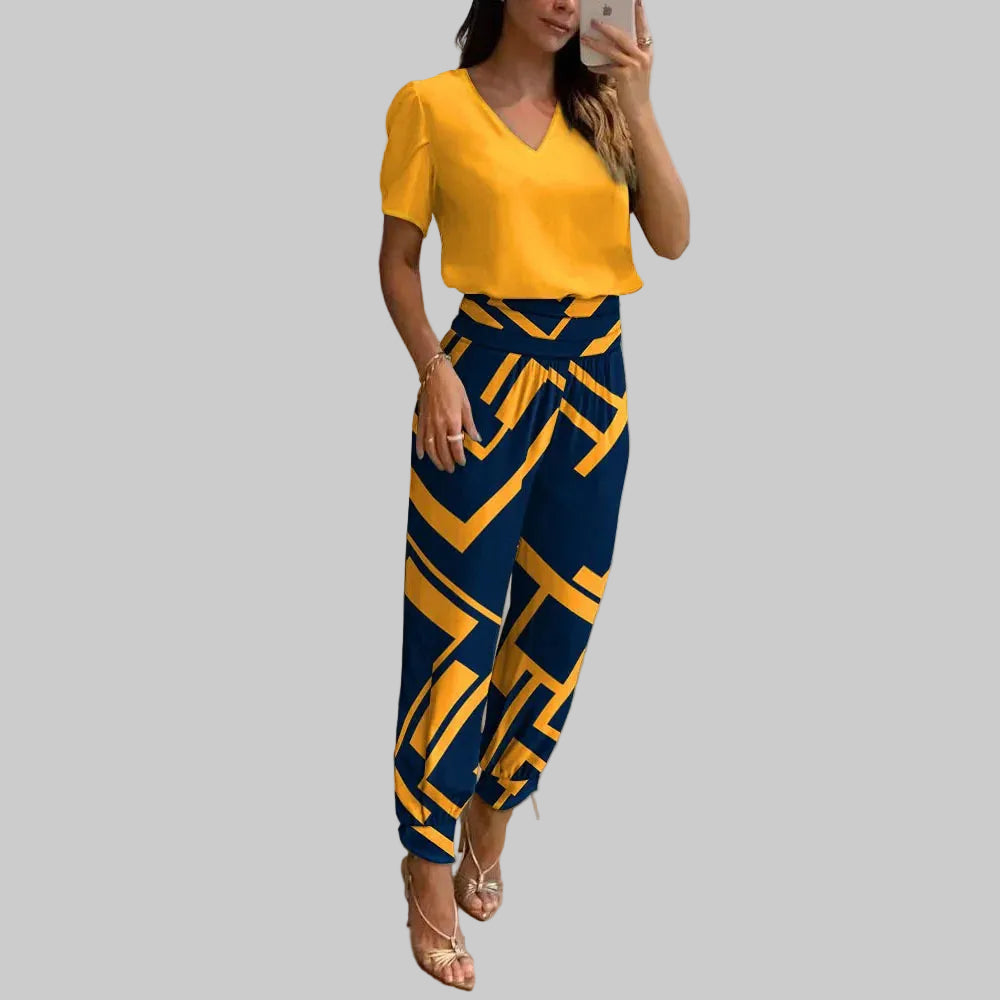 Woman taking a mirror selfie wearing a yellow top and blue patterned pants in a modern interior setting.