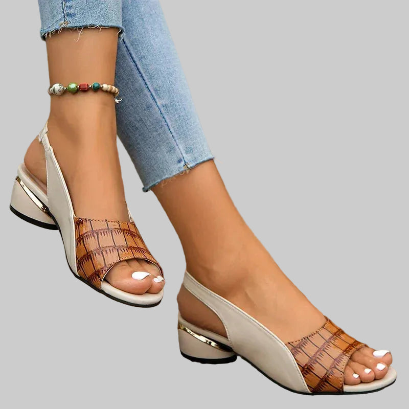 Close-up of a person wearing brown and white open-toe sandals on a wooden floor.