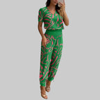 Woman taking a mirror selfie wearing a green and pink patterned outfit in a modern room.