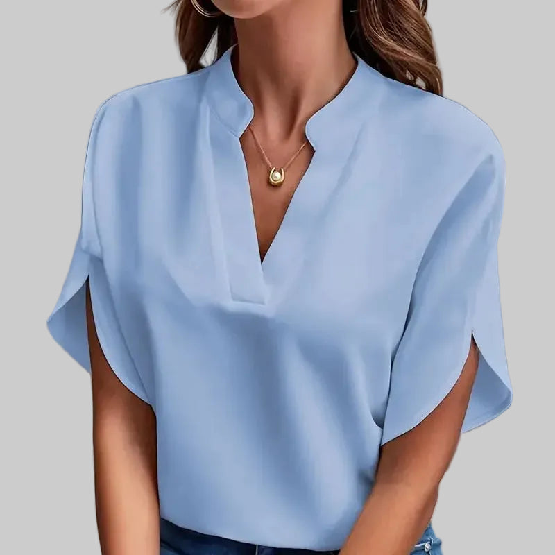 Woman wearing a light blue blouse and jeans against a gray background