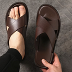 Brown sandals being held by a hand on a dark gray background