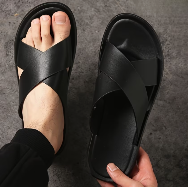Black sandals being held up on a dark background